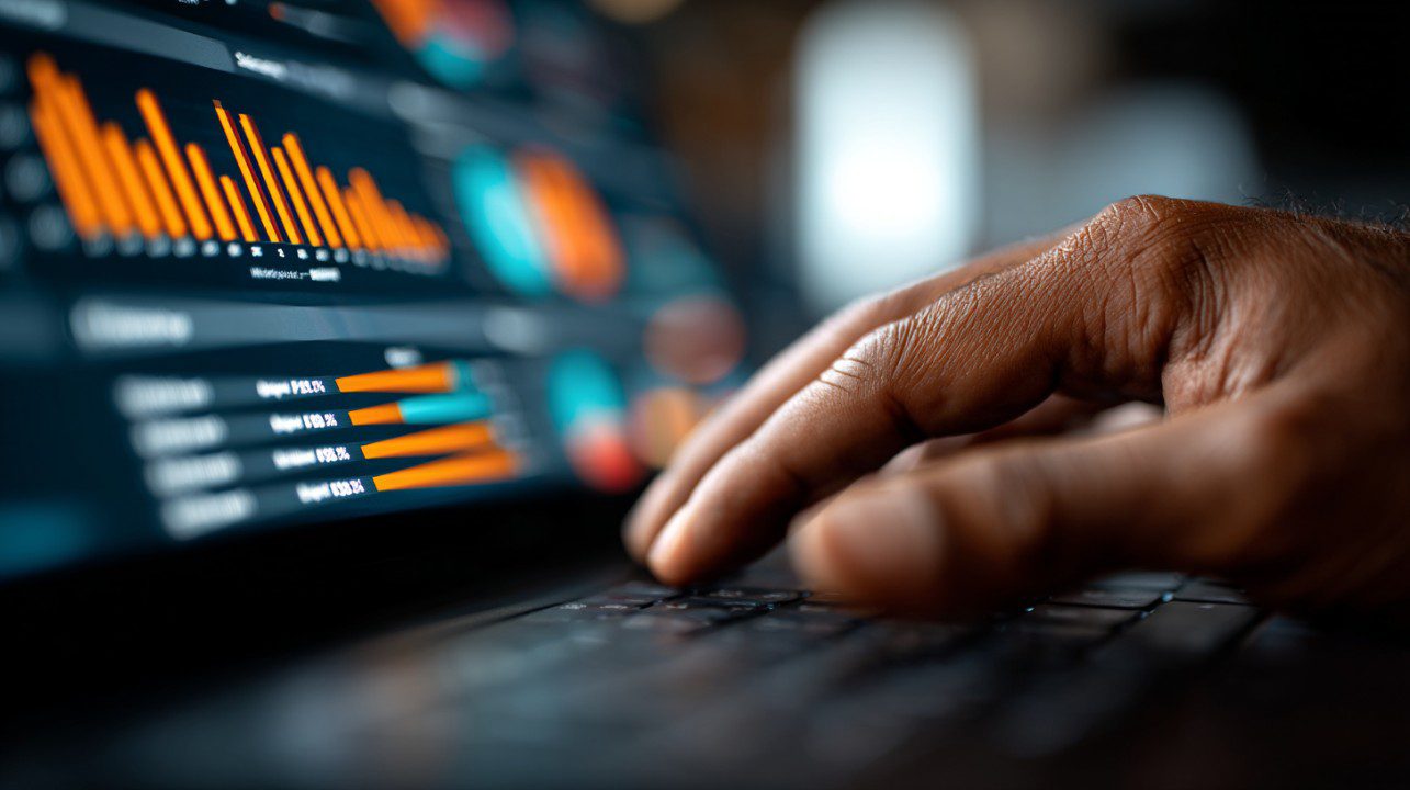 Close-up of dark-skinned hands working on a laptop displaying analytics charts